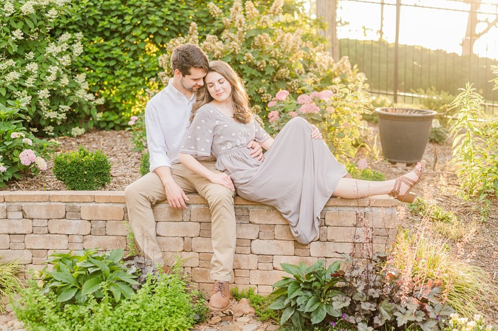 couple sitting on wall in the gardens during engagement session at tanglewood